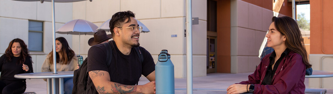 Two pima students chat at an outside table in a courtyard at Pima's Northwest Campus