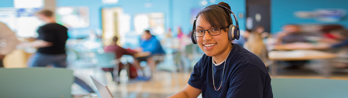 Smiling student sits and works on her computer in a student lounge