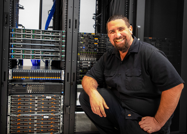 An IT student poses smiling infront of student run servers in a server room on campus