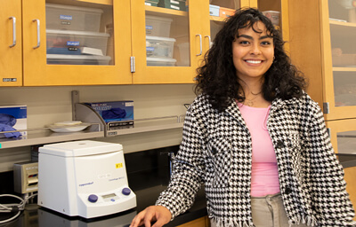 Briana Pomales stans next to a centrifuge in a chem classroom