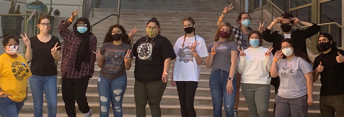 A Student club stands, wearing masks, on the steps of northwest campus. 