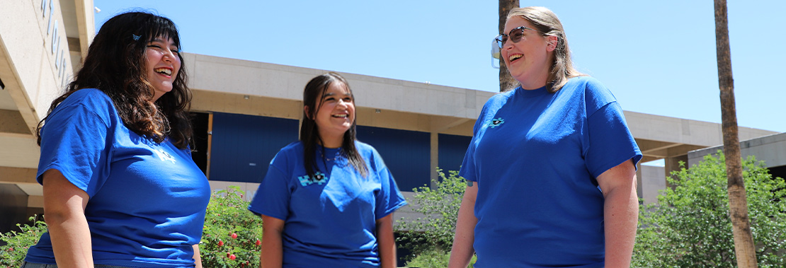 Three Peer Mentors stand smiling and laughing in a breezeway at West Campus