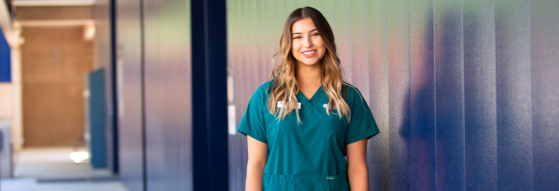 Image of Brianna Sandate in nursing scrubs in front of a building at West Campus