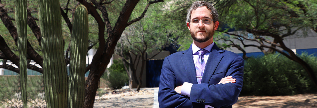 Shane Gardiner stands confidently in a suit on a walkway at West Campus