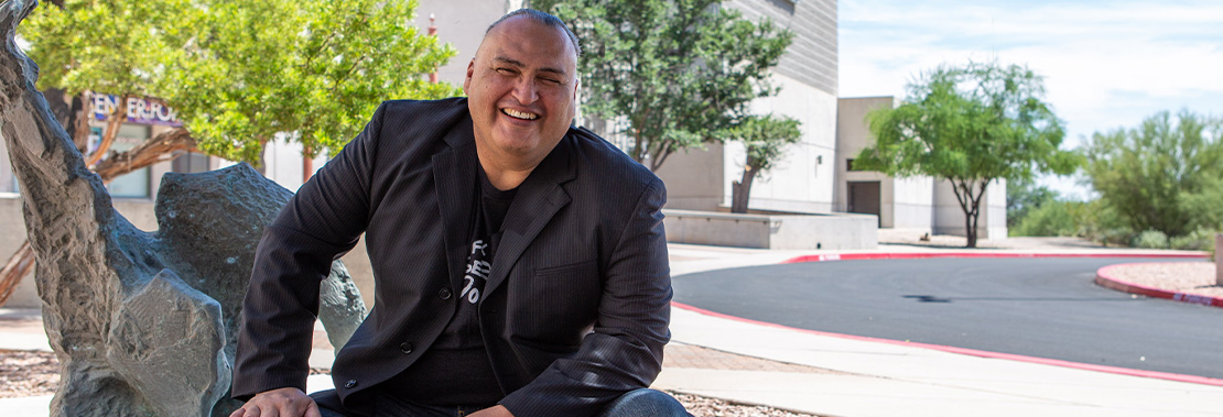 Jon Proudstar sits next to a statue outside of the Center for Arts Center at Pima West Campus