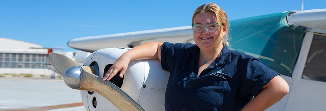 Suzanne Roy stands propped up smiling against a small plane