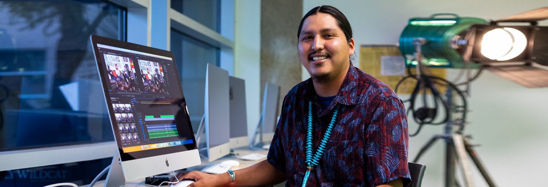 Luke Hunt sits in a video lab at West Campus smiling. 