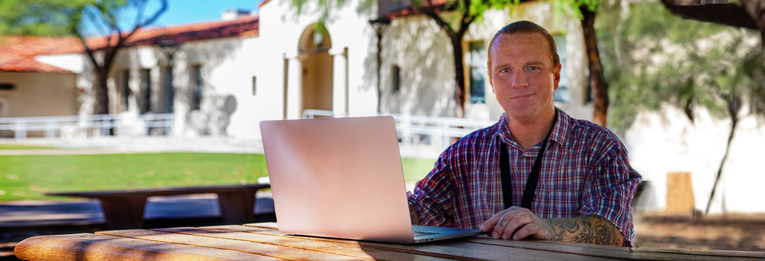 Peter Keith Sits at a table outside of Downtown Campus with a laptop