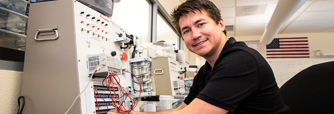 Tony Lopez smiles while working on a device in the AIT Lab at West Campus