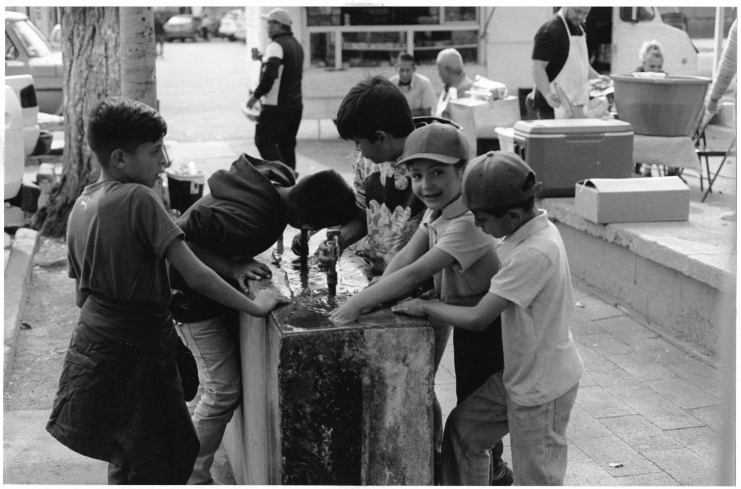 A black and white photograph of 5 kids drinking from a water fountain