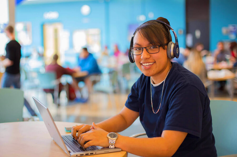 A student smiles while working on her computer in a student lounge