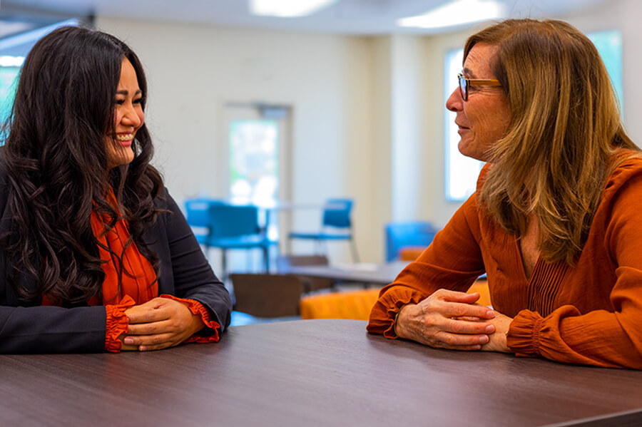 A student and instructor talk in a student lounge at Pima West Campus