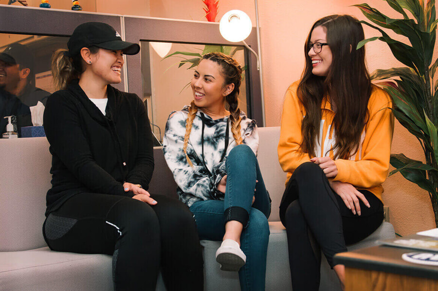 Three students sit in a student lounge smiling and laughing