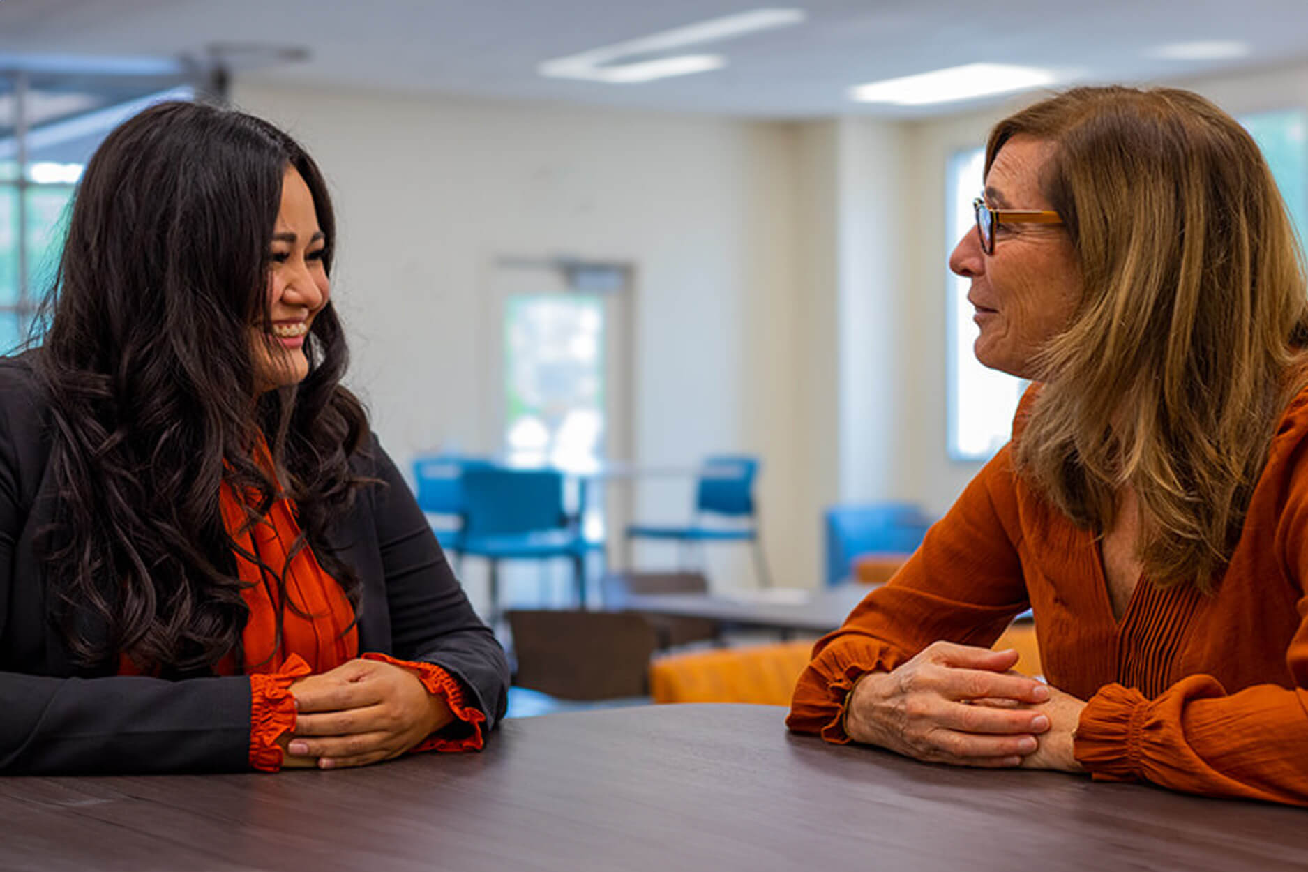 A student and teacher sit smiling in a campus lounge