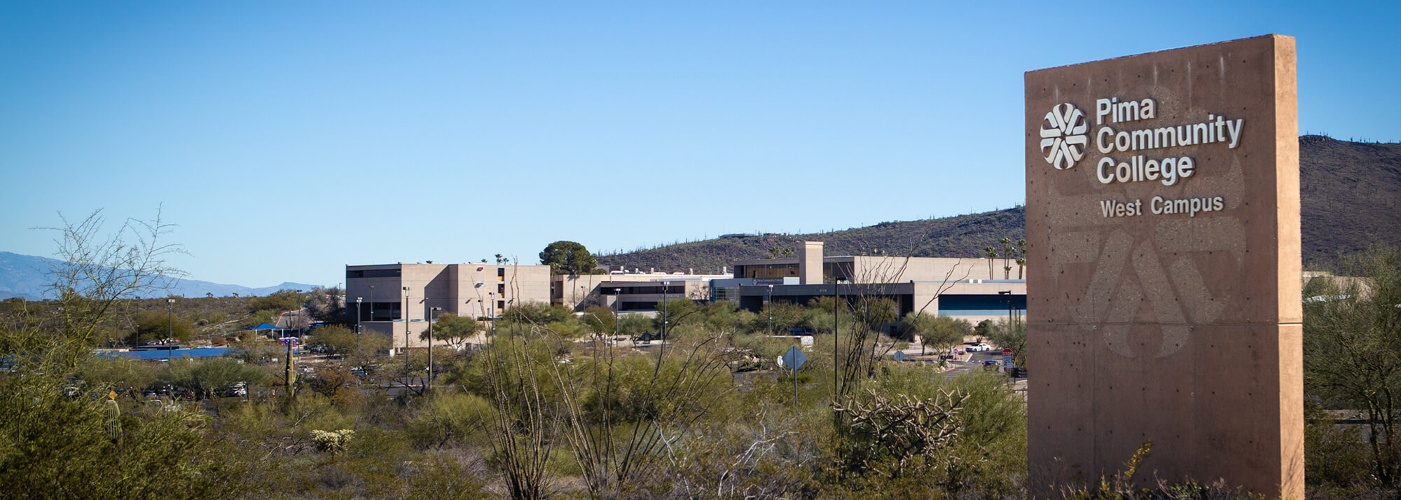 An outside shot of the PCC West Campus sign with the westcampus in the landscape in the background.