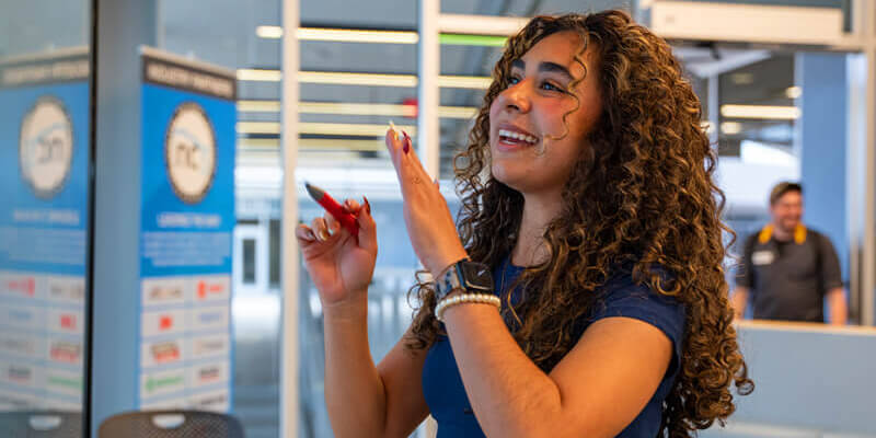 A female student smiles and talks through work she is doing on a white board in a campus study room.