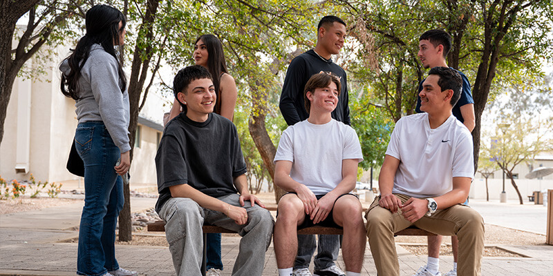 A group of students sit on a bench outside of downtown campus.