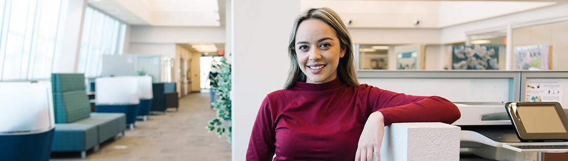 A student poses and smiles in a study area at a campus