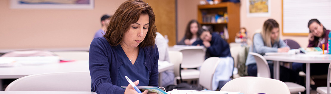 A student raises her hand in a Pima classroom with students interacting with each other