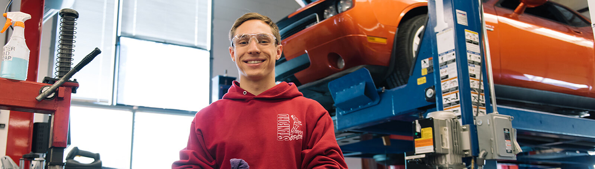 An automotive student stands smiling in front of a vehicle in the Automotive Technology and Innovation Center