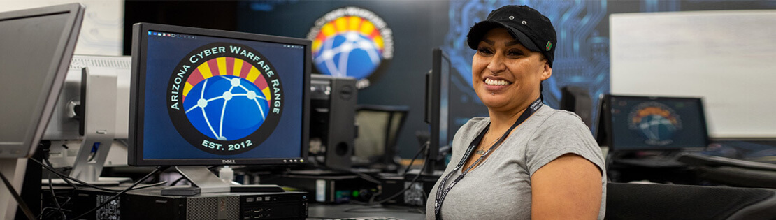 A student sits smiling at a computer in Pima's Cyber Warfare Range class