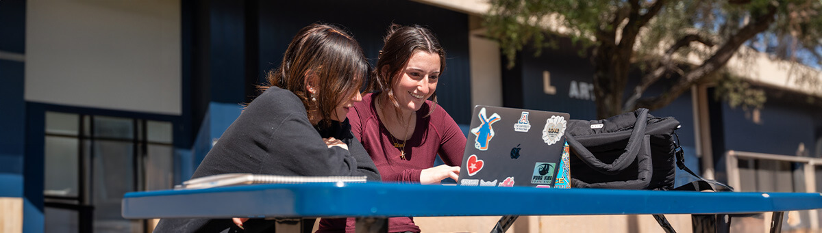 Students sits at a table in a breezeway on a laptop
