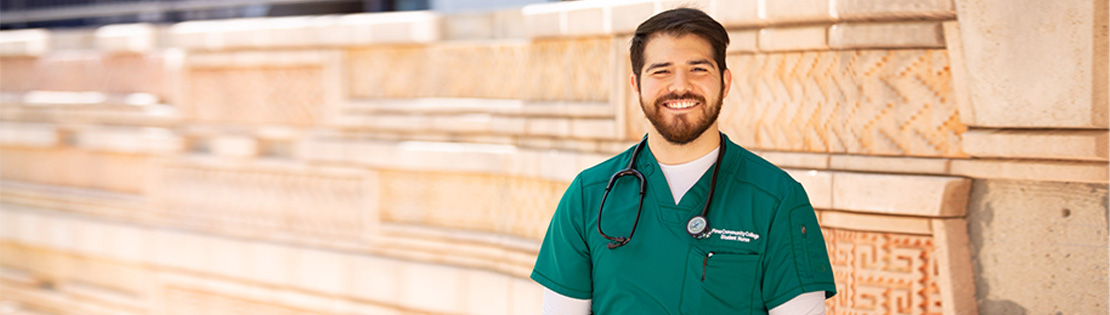 A Pima nursing student stands smiling against a wall at Pima's West Campus