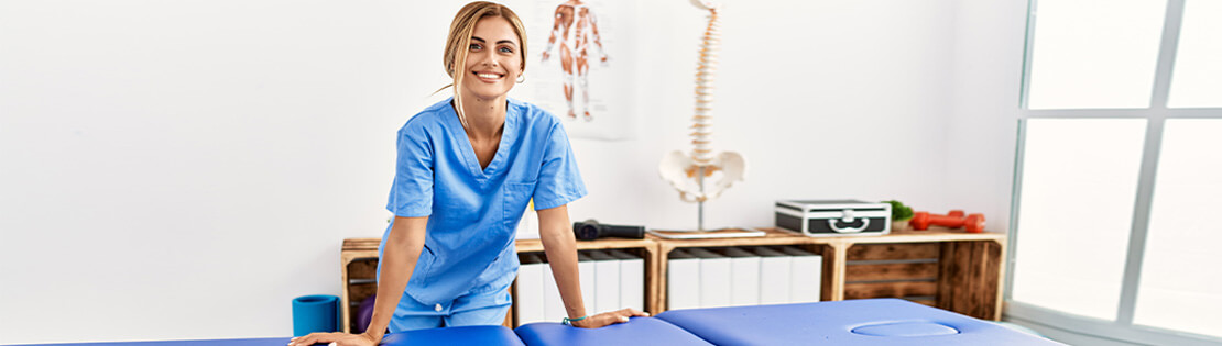 A massage therapist smiles in front of her table