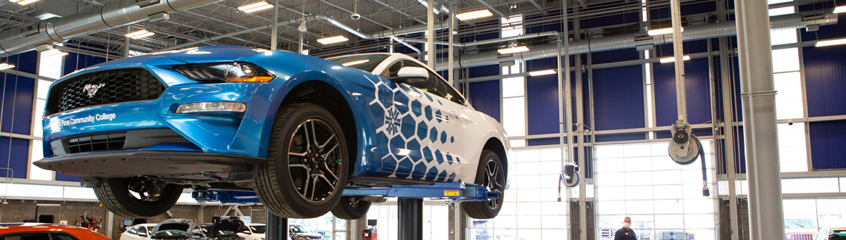 A student in automotive program poses and smiles while working on a vehicle on a lift