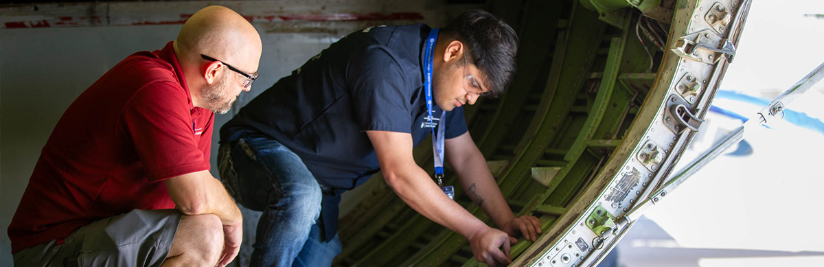 An aviation student works on inside a plane's body on the structure