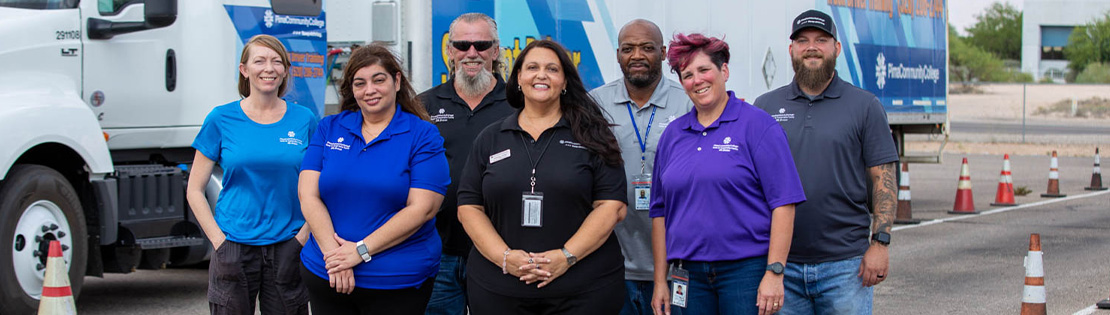 Pima's truck driving faculty and staff stand in front of a Pima truck posing for a photo