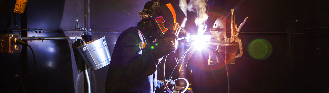 A student pauses and poses for a photo while working on welding project