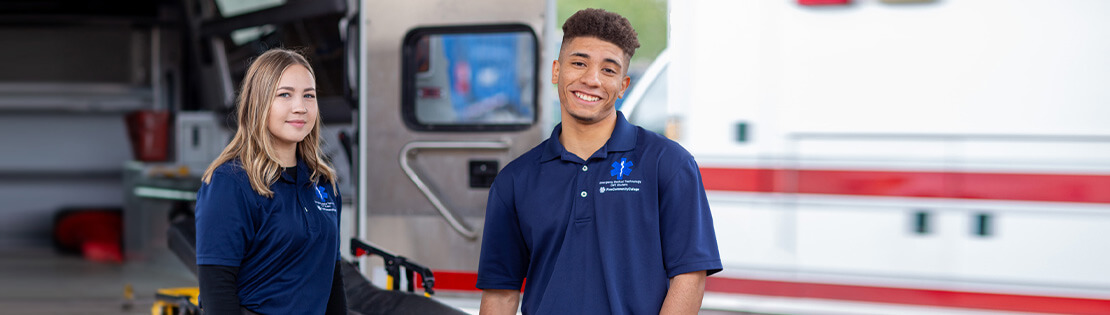 Two EMT students smile and pose in the back of an ambulance