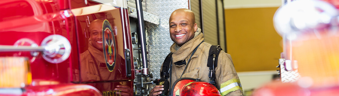 A firefighter poses smiling in gear on a fire engine