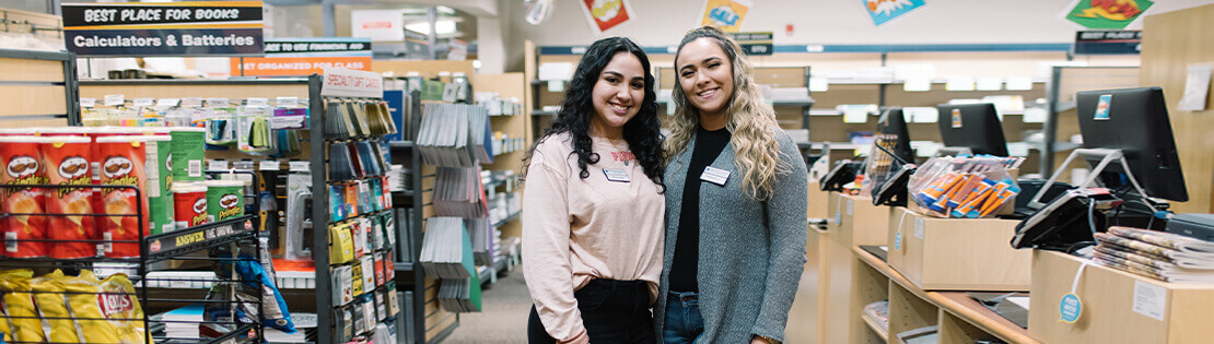 Two Student workers stand smiling in a Pima Bookstore