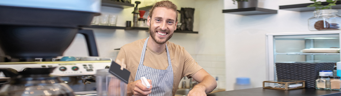 A Small business owner stands smiling behind his coffee counter