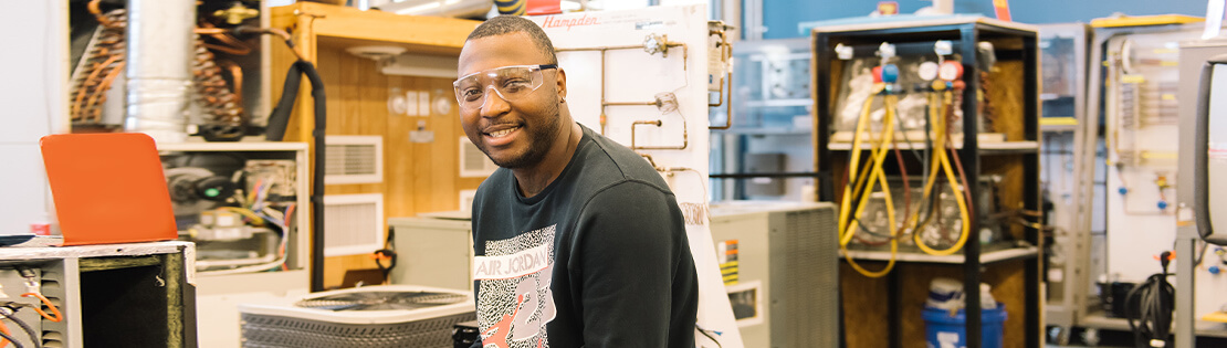 A student sits smiling with safety glasses in an engineering lab