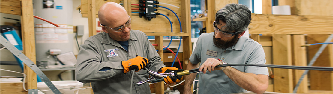 An older student and a teacher work on an electrical equipment