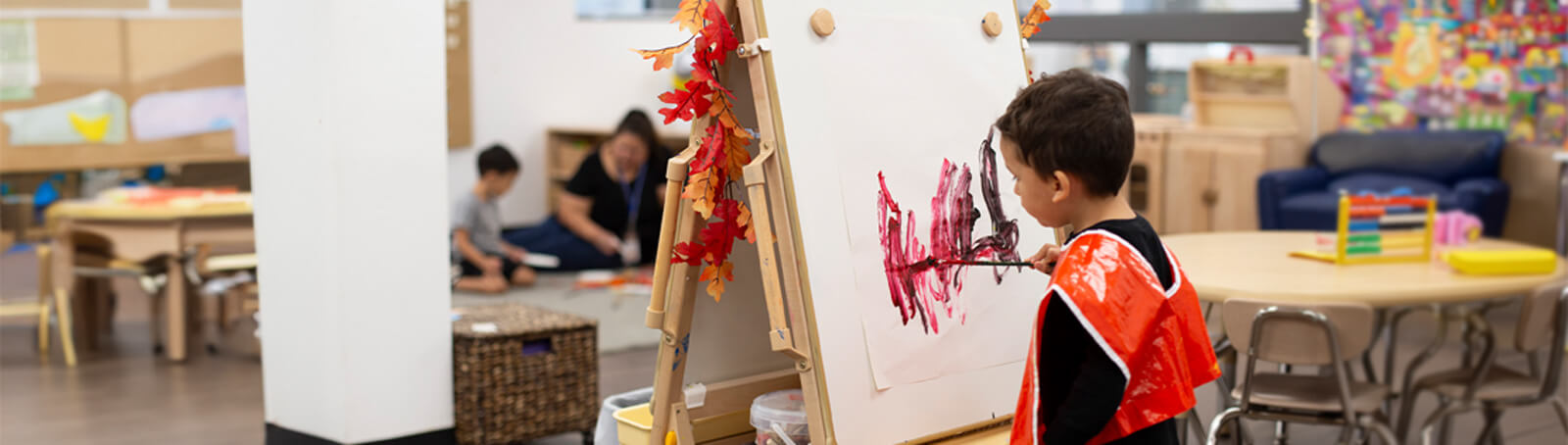 A young Child sits and smiles in a preschool classroom iwth his teachers